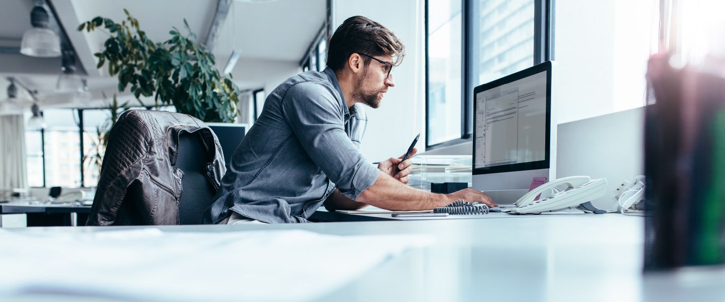 Junger Mann sitz am Schreibtisch vor seinem Computer.