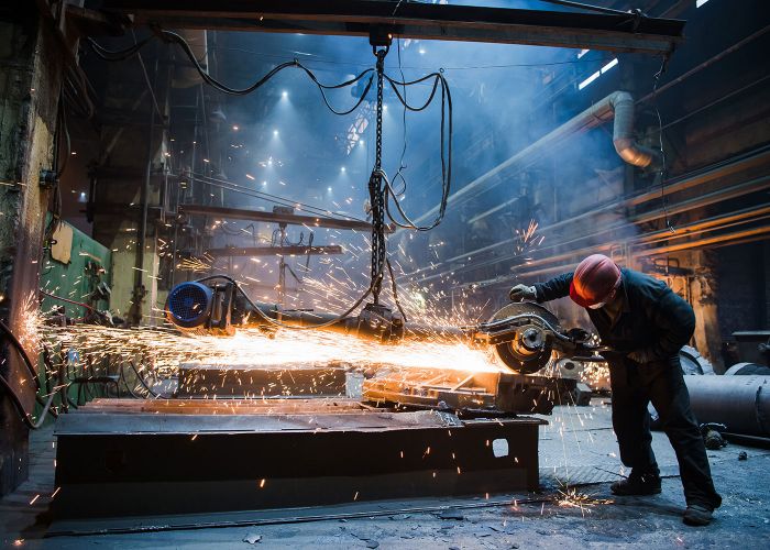 Arbeiter bei der Metallverarbeitung mit einem Winkelschleifer in einer Werkshalle.