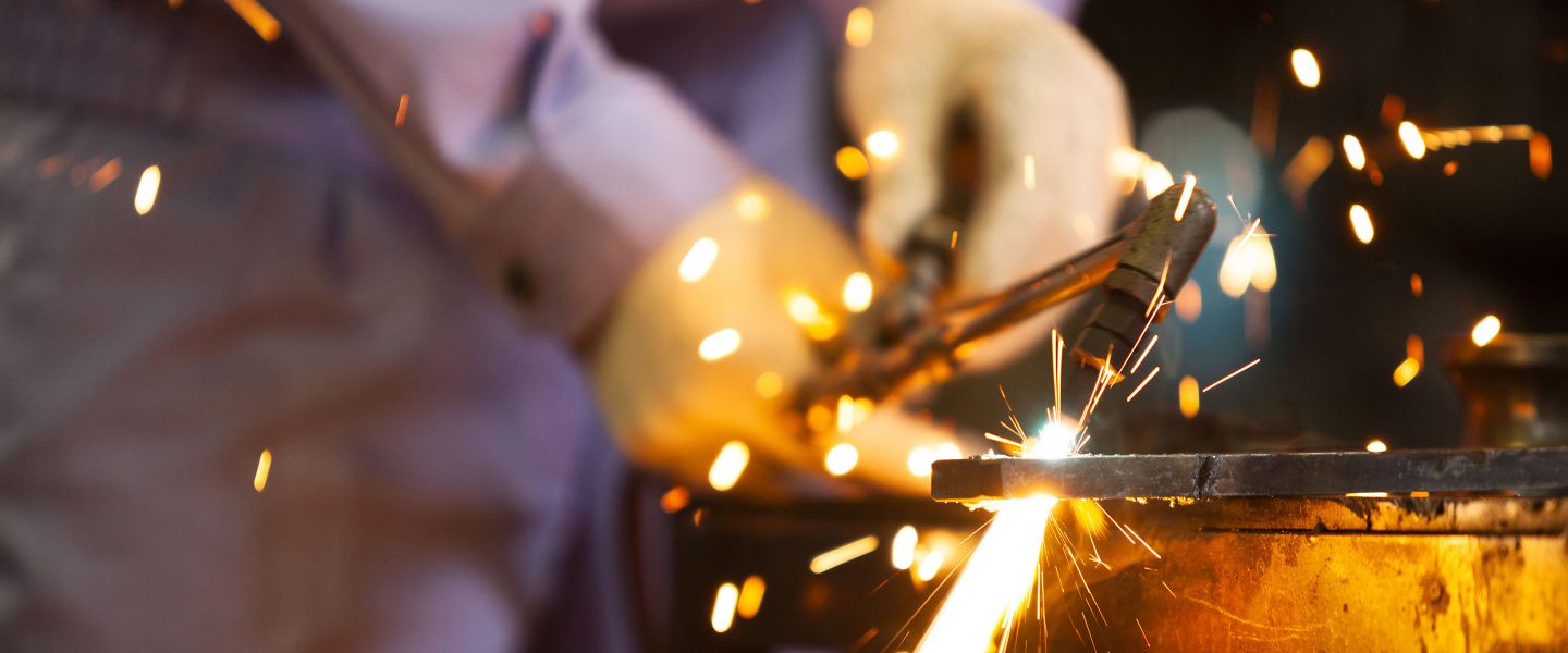 Person in Schutzkleidung arbeitet mit einer Lichtbogenschweißmaschine und erzeugt einen Funkenflug.